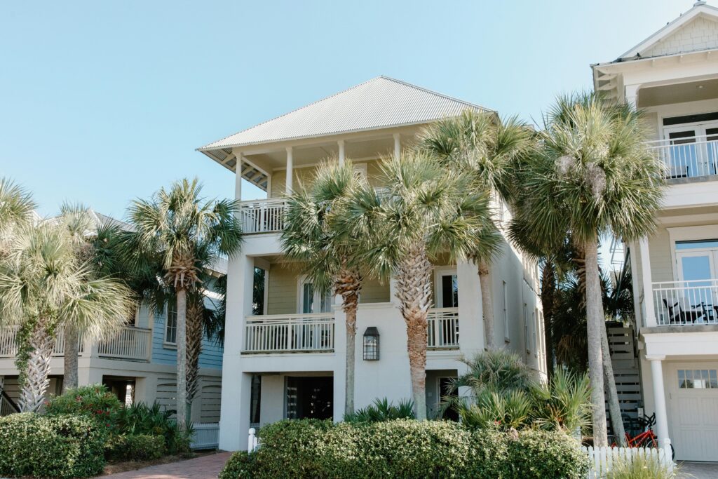 Sunny beach house exterior surrounded by lush palm trees and blue sky.