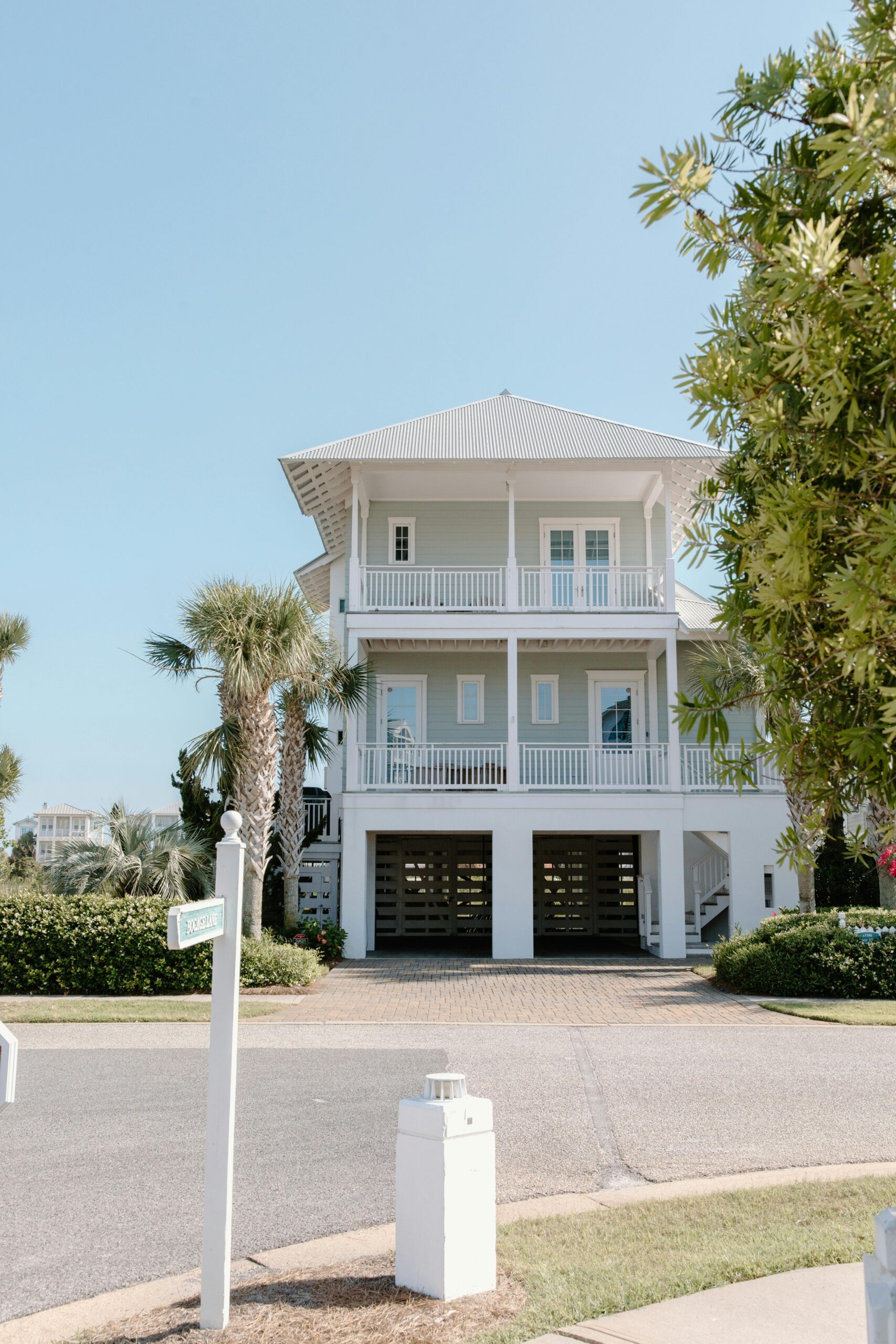 Elegant coastal house with palm trees and clear sky, perfect for real estate and architecture themes.